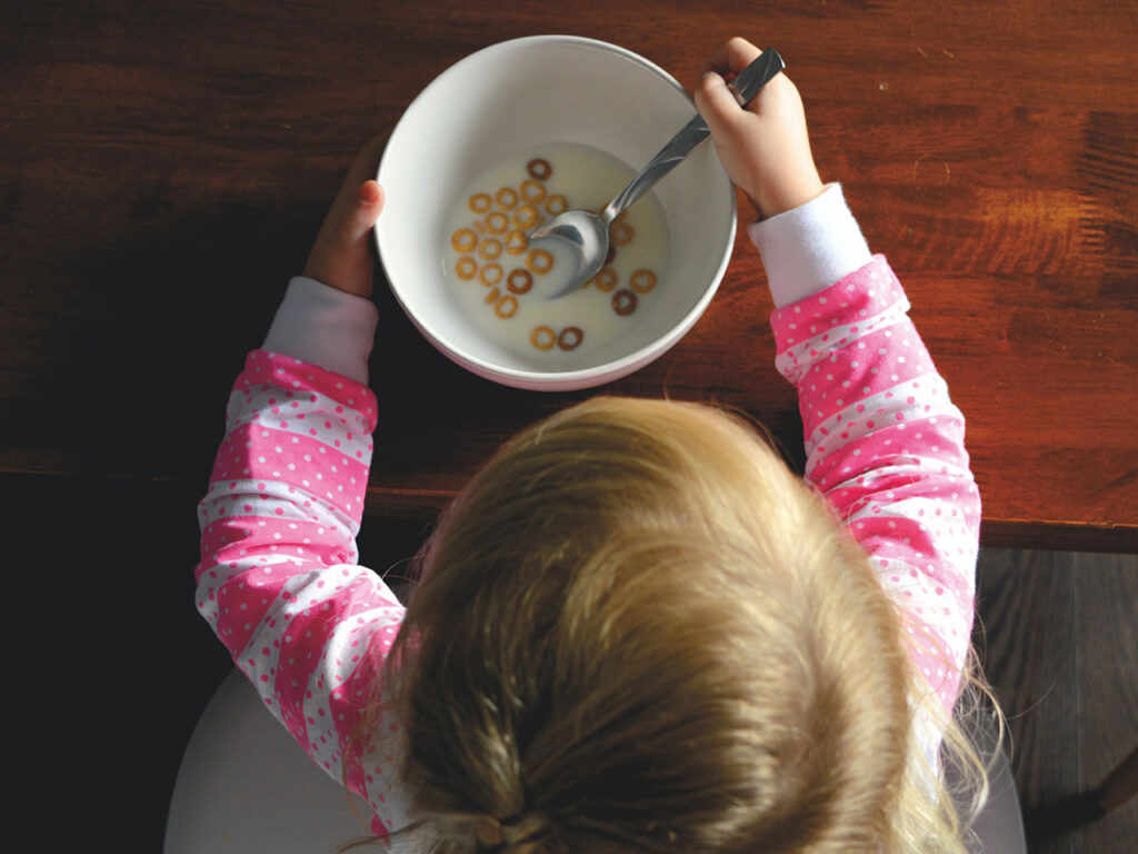 Barn äter flingor med mjölk ur skål